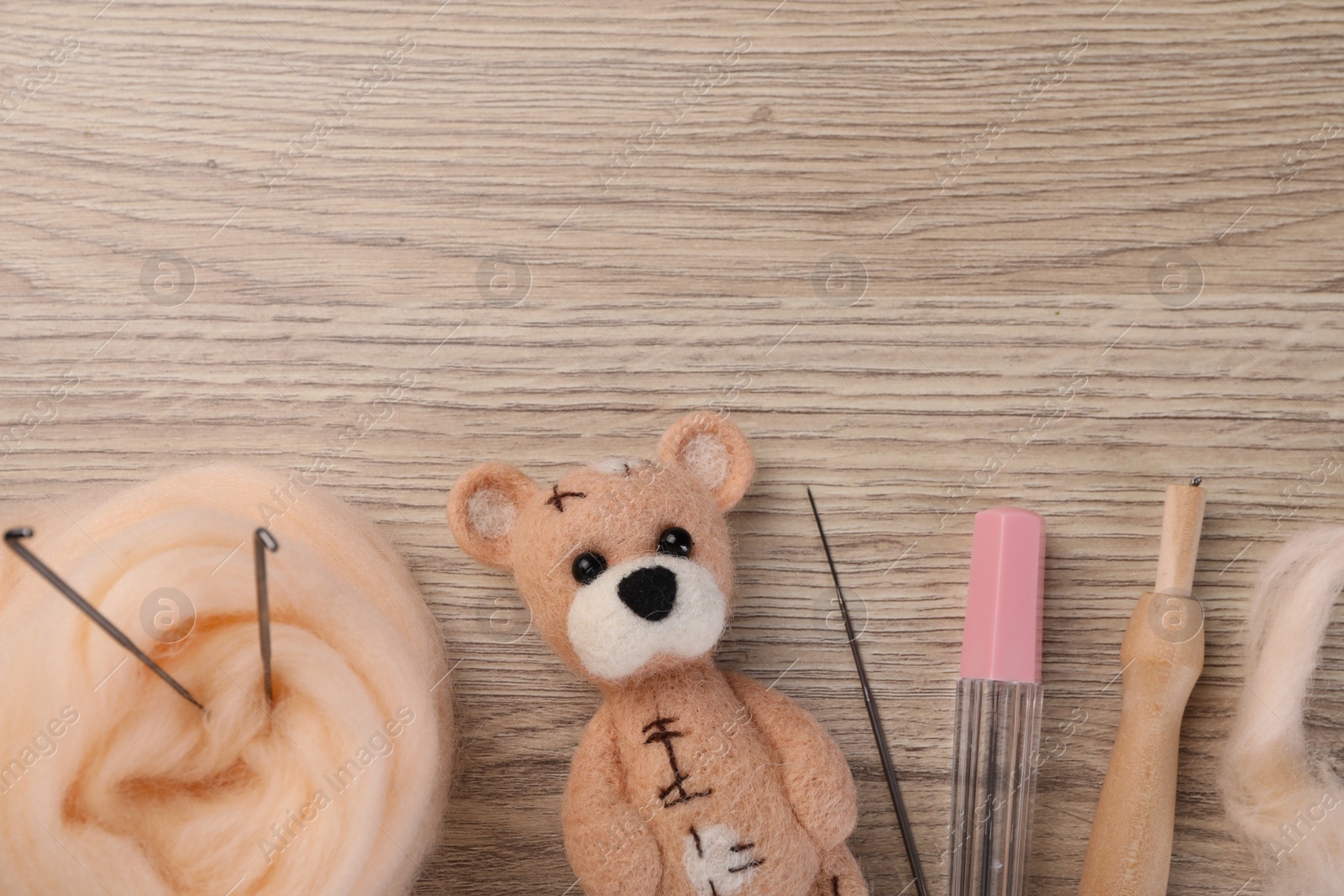 Photo of Felted bear, wool and tools on wooden table, flat lay. Space for text