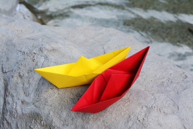 Photo of Beautiful yellow and red paper boats on stone near water outdoors