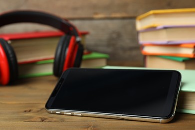 Photo of Modern smartphone with blank screen and books on wooden table, closeup. Space for design