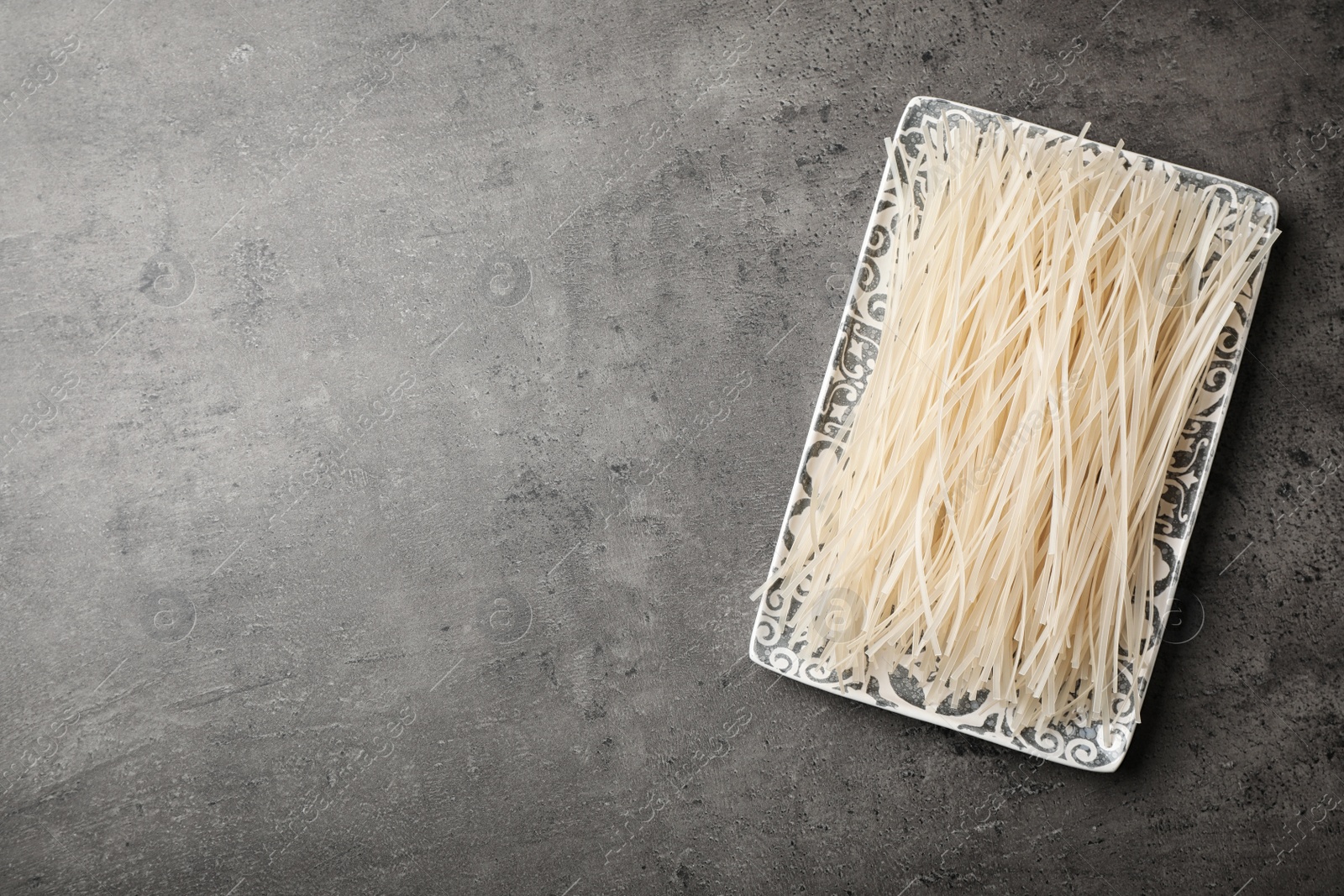 Photo of Plate with raw rice noodles on grey background, top view. Space for text