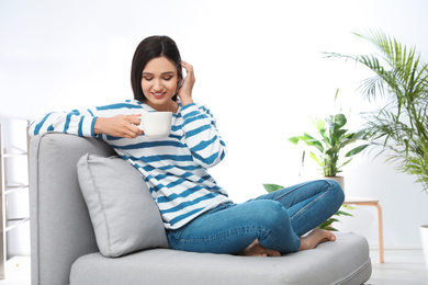 Photo of Young woman with cup of drink relaxing on couch at home