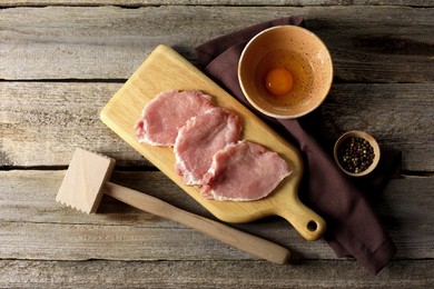 Photo of Cooking schnitzel. Raw pork slices, egg, peppercorns and meat tenderizer on wooden table, flat lay