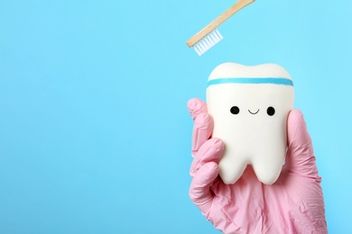Photo of Dentist holding model of tooth with cute face and wooden brush on color background, space for text