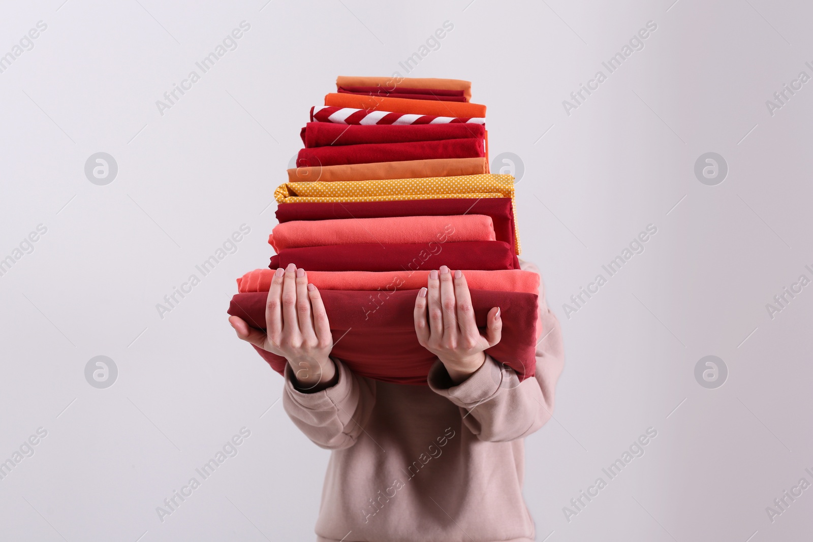 Photo of Woman holding stack of clean bed linens on light background