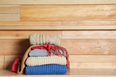 Photo of Stack of winter clothes against wooden background. Space for text