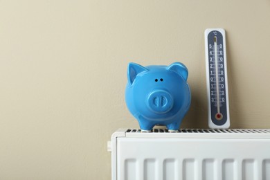 Photo of Piggy bank and thermometer on heating radiator against beige background, space for text