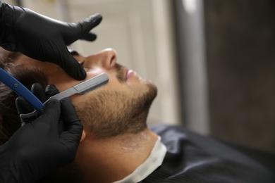 Professional hairdresser shaving client with straight razor in barbershop