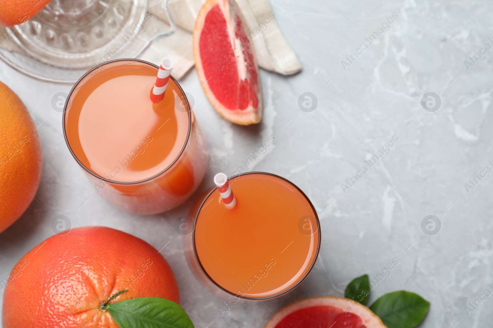 Photo of Tasty freshly made grapefruit juice and fruits on light grey marble table, flat lay. Space for text