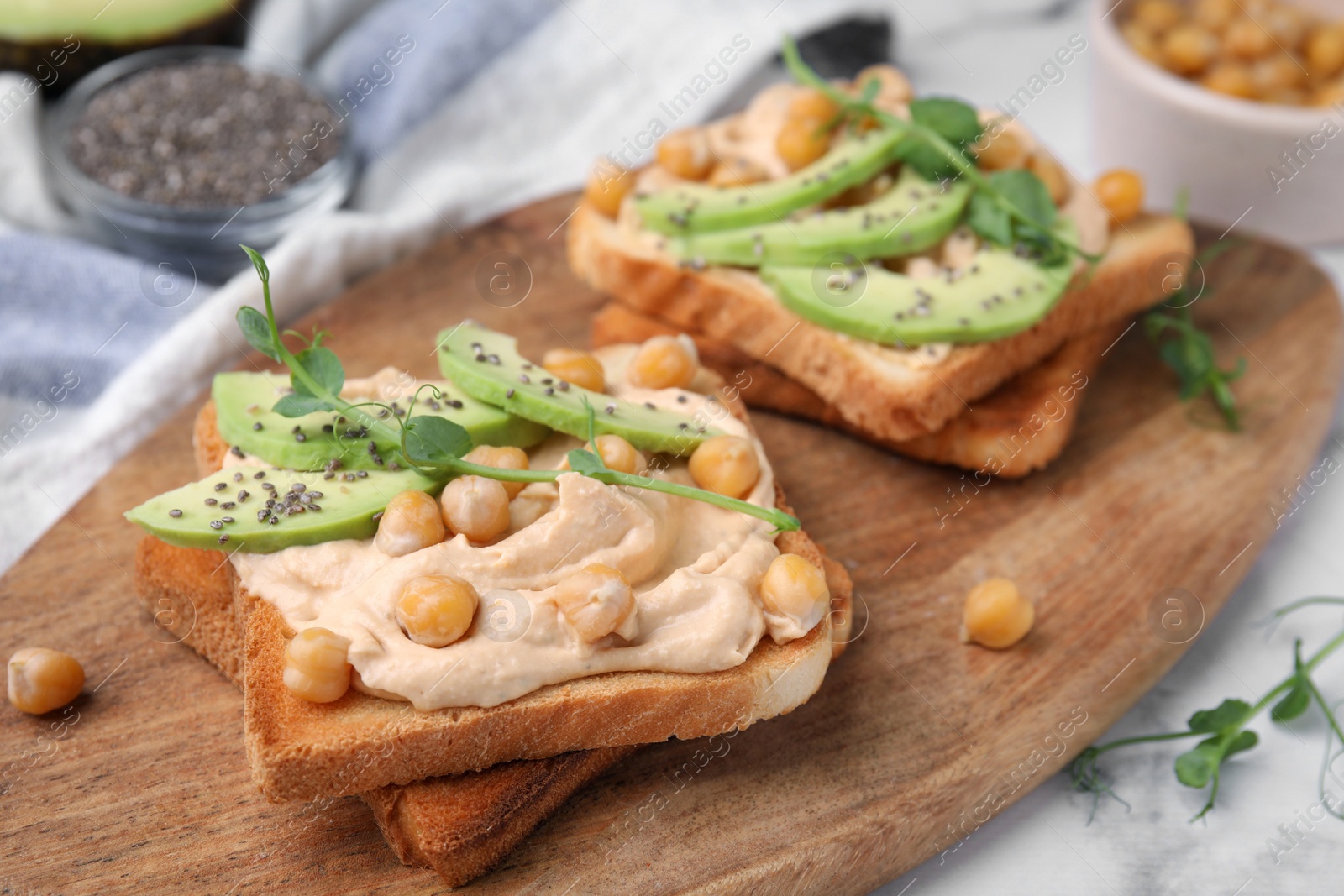 Photo of Delicious sandwiches with hummus, avocado and chickpeas on wooden board