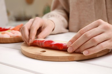 Woman making delicious spring roll at white wooden table, closeup