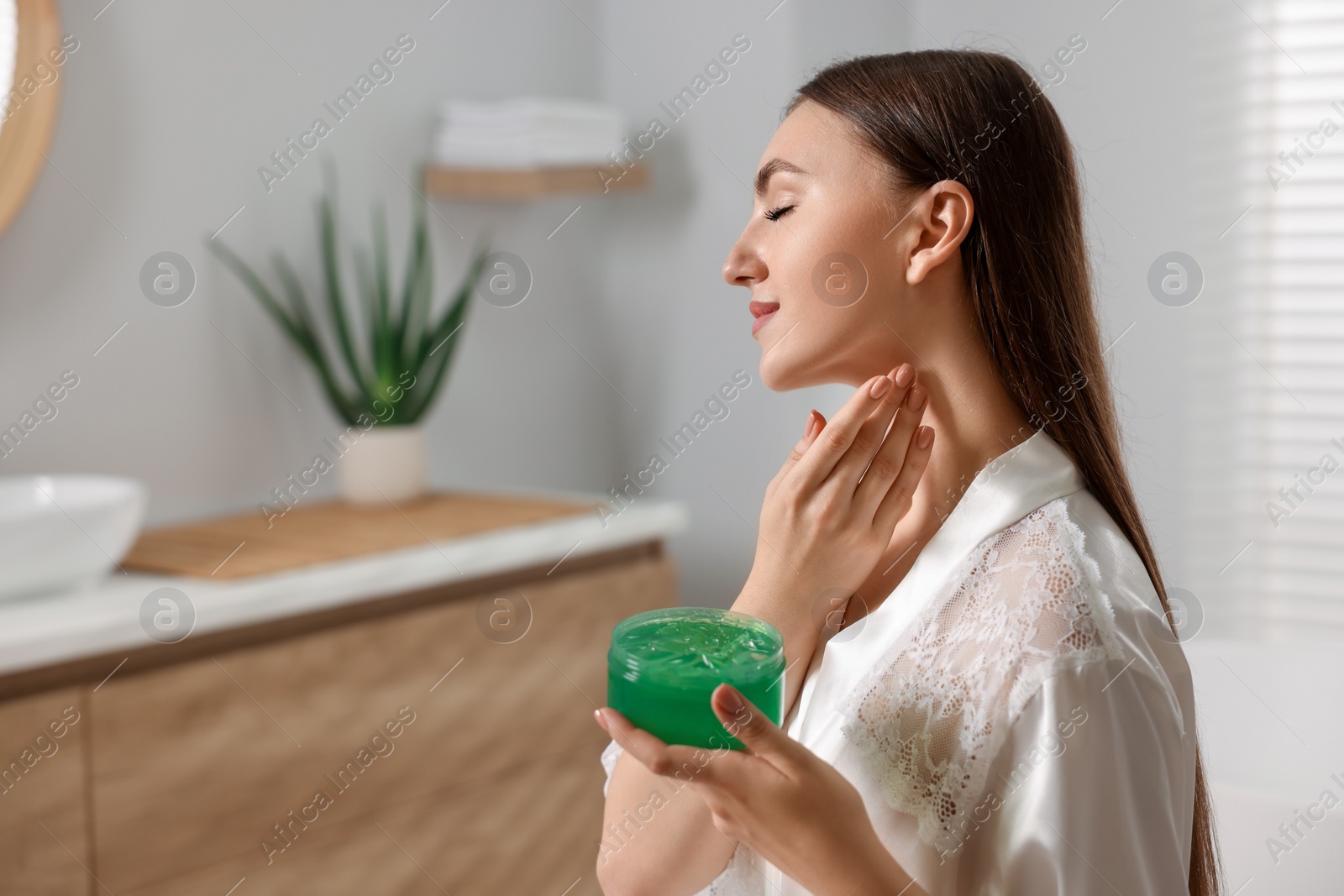 Photo of Young woman applying aloe gel onto her neck in bathroom. Space for text