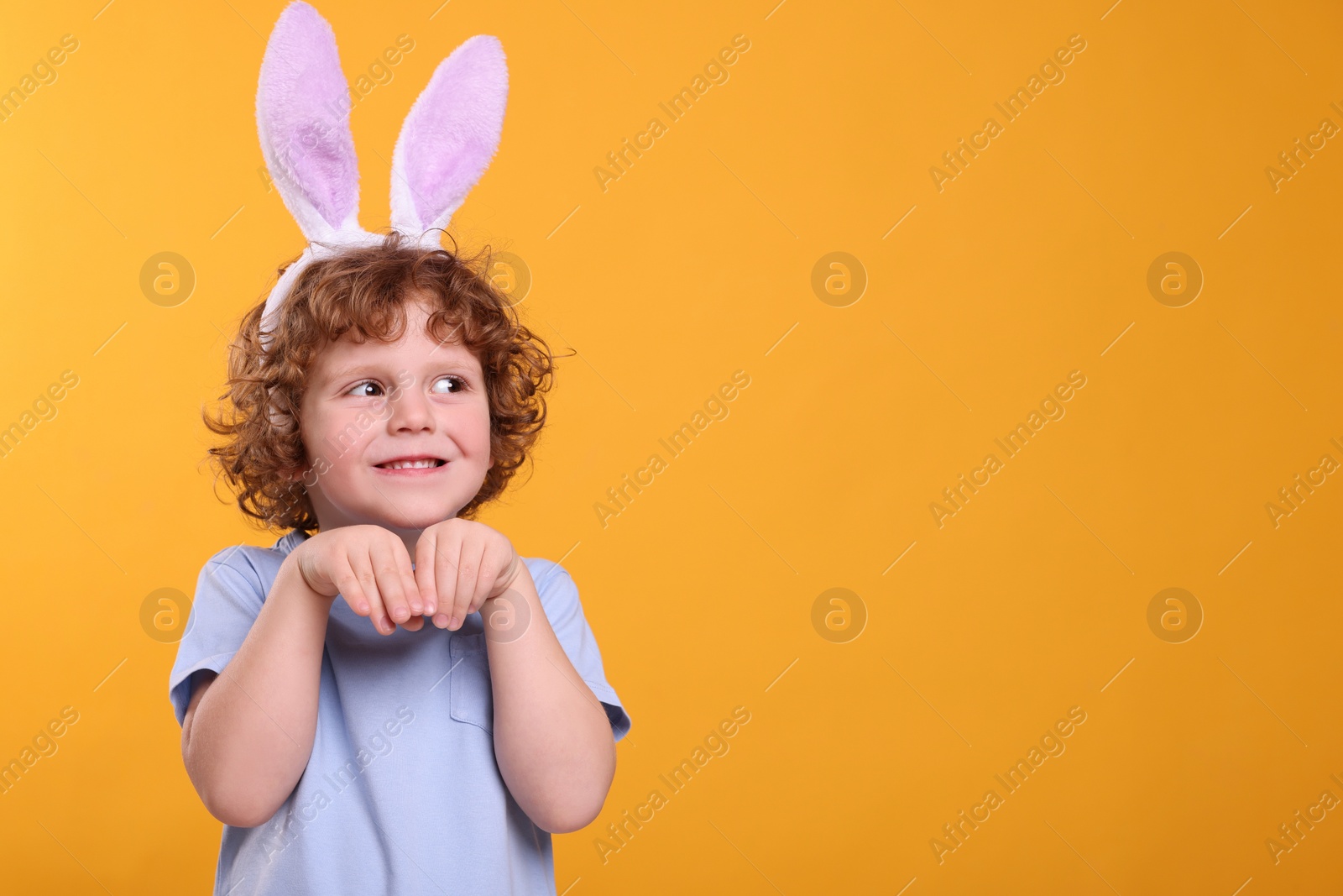 Photo of Happy boy wearing cute bunny ears headband on orange background, space for text. Easter celebration