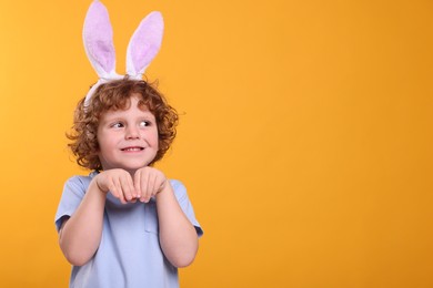 Happy boy wearing cute bunny ears headband on orange background, space for text. Easter celebration