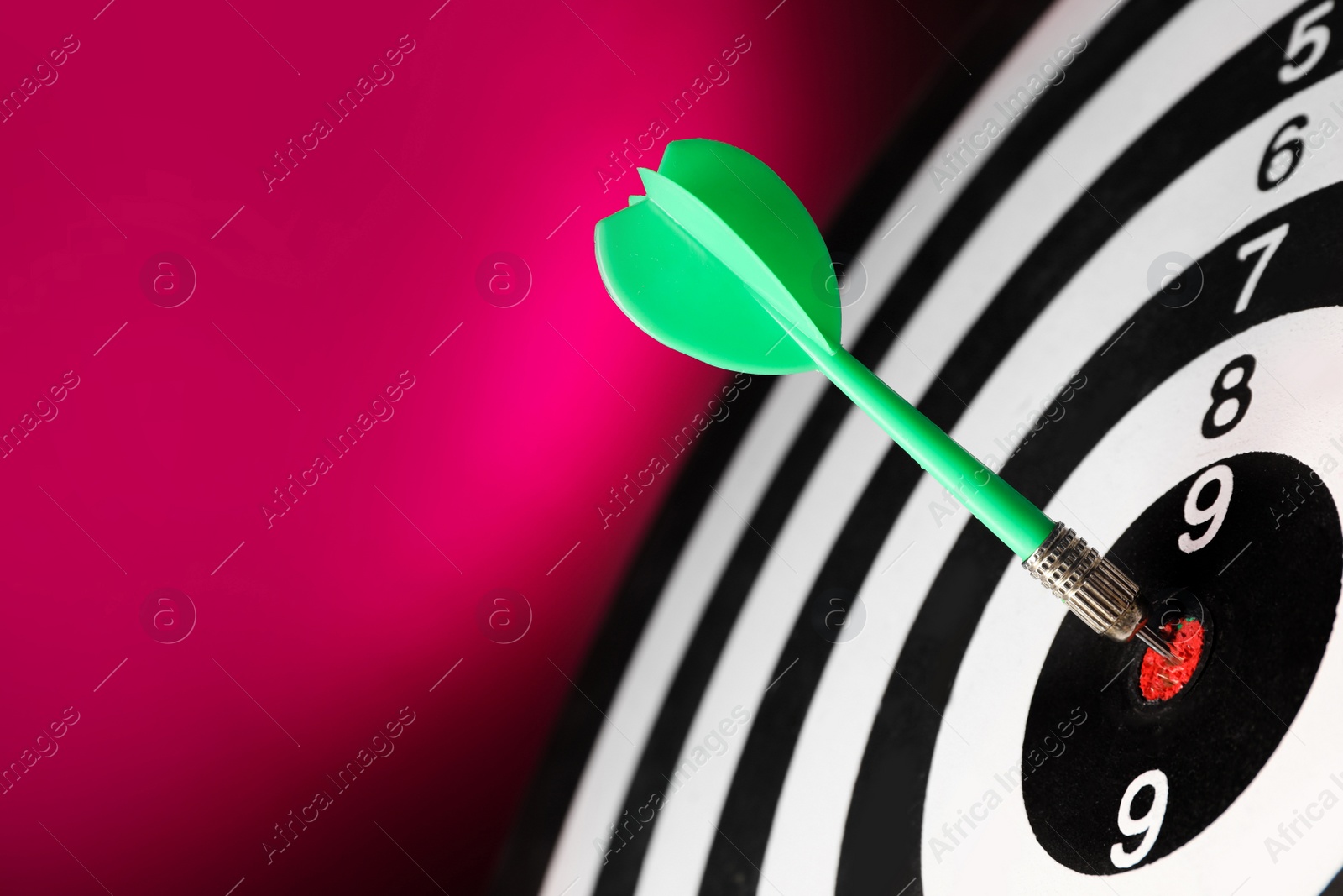 Photo of Green arrow hitting target on dart board against magenta background