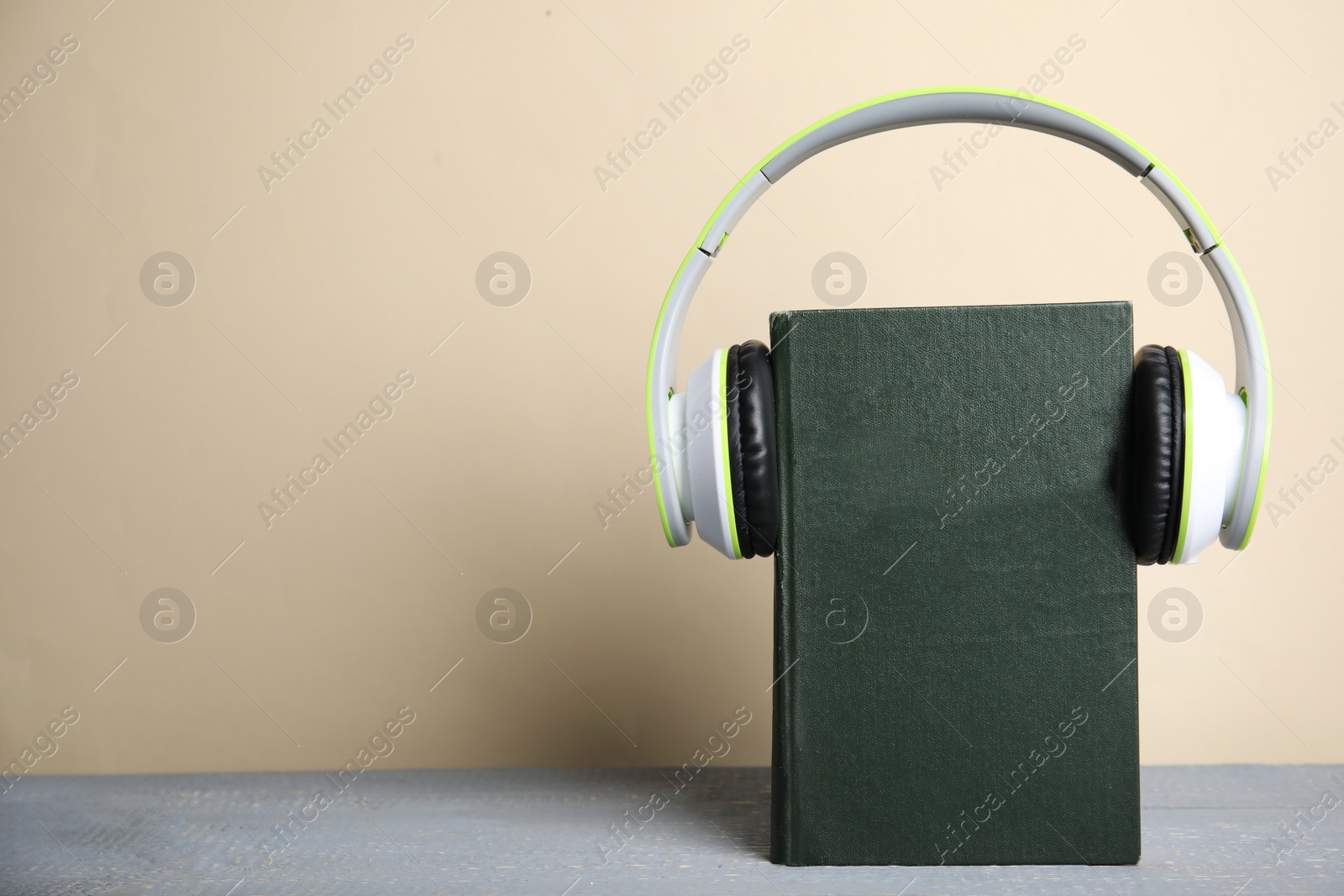 Photo of Book and modern headphones on grey wooden table. Space for text