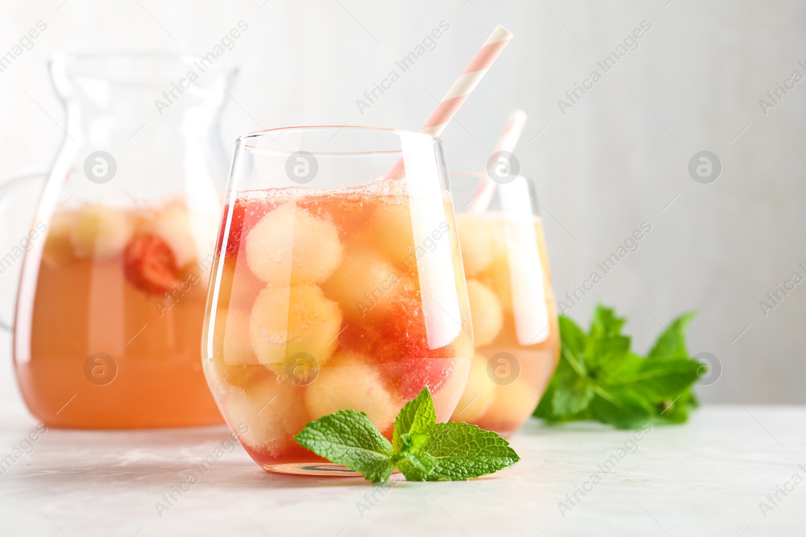 Photo of Glasses of melon and watermelon ball cocktail with mint on white table