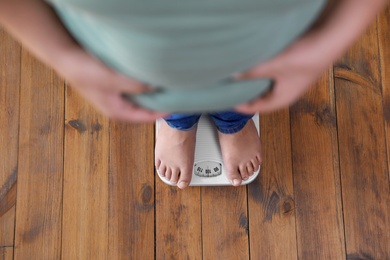 Photo of Overweight boy standing on floor scales indoors, above view