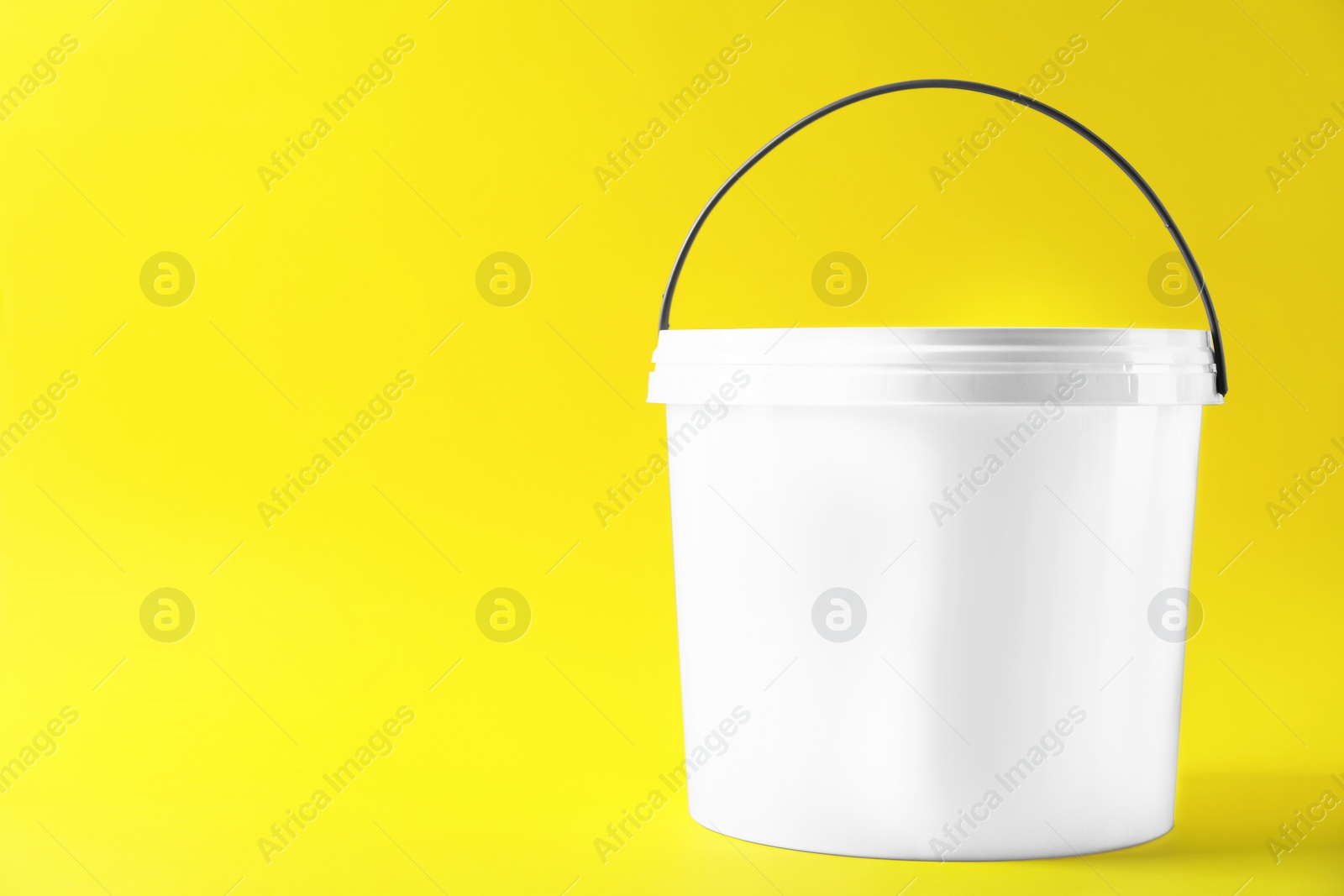 Photo of One plastic bucket with lid on yellow background. Space for text