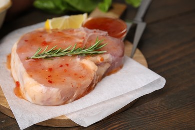 Board with raw marinated meat and rosemary on wooden table, closeup
