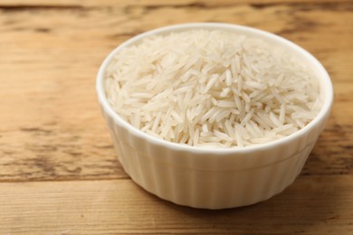 Photo of Raw basmati rice in bowl on wooden table, closeup
