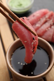 Photo of Dipping tasty sashimi (piece of fresh raw tuna with sesame seeds) into soy sauce at table, closeup