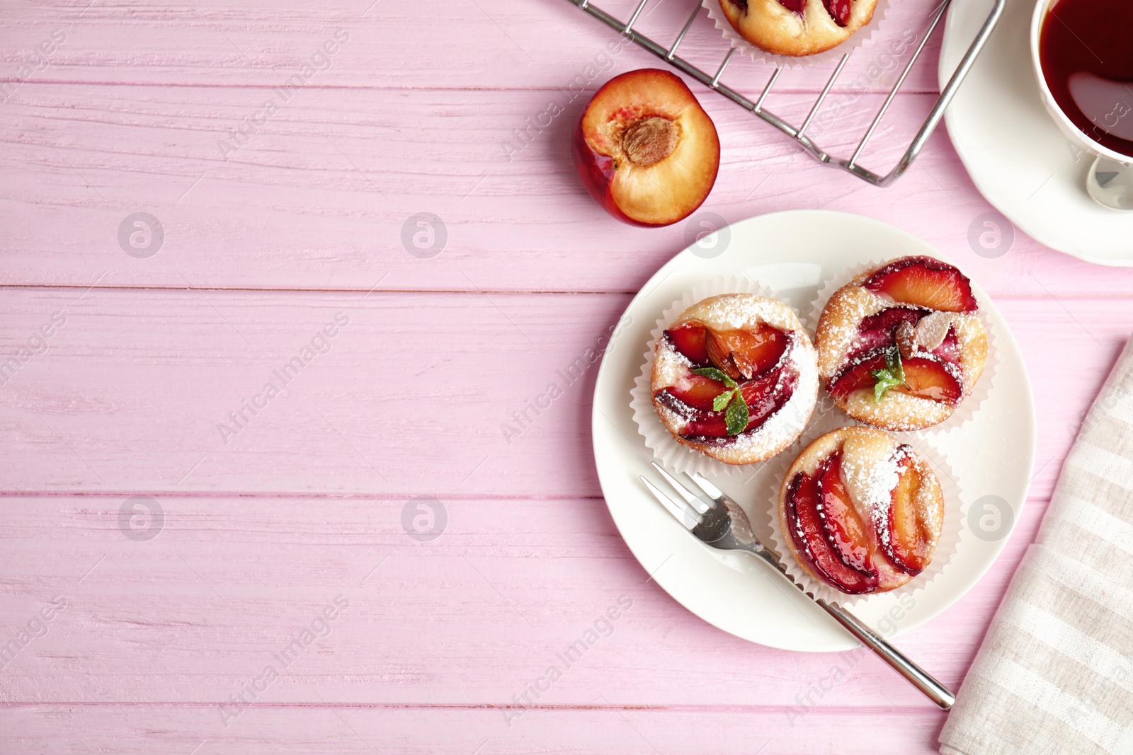 Photo of Delicious cupcakes with plums on pink wooden table, flat lay. Space for text