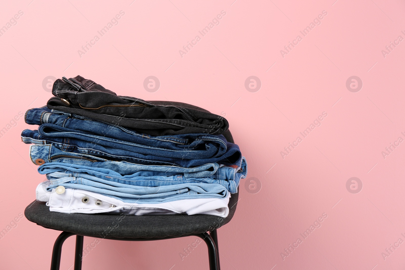 Photo of Stack of different jeans on stool against color background