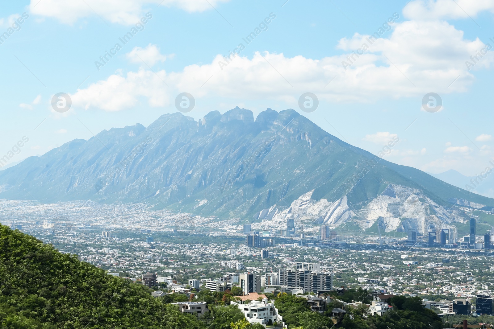 Photo of Picturesque view of trees, buildings and mountains under beautiful sky in city