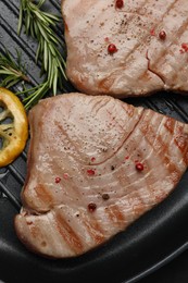 Photo of Delicious tuna steaks, lemon and rosemary in grill pan, top view