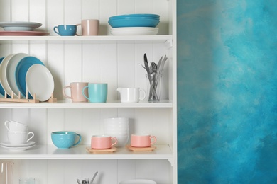 Photo of White shelving unit with set of dishware near color wall. Space for text