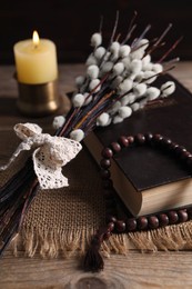 Photo of Rosary beads, Bible, burning candle and willow branches on wooden table, closeup