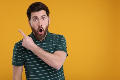 Photo of Surprised man pointing at something on yellow background, space for text