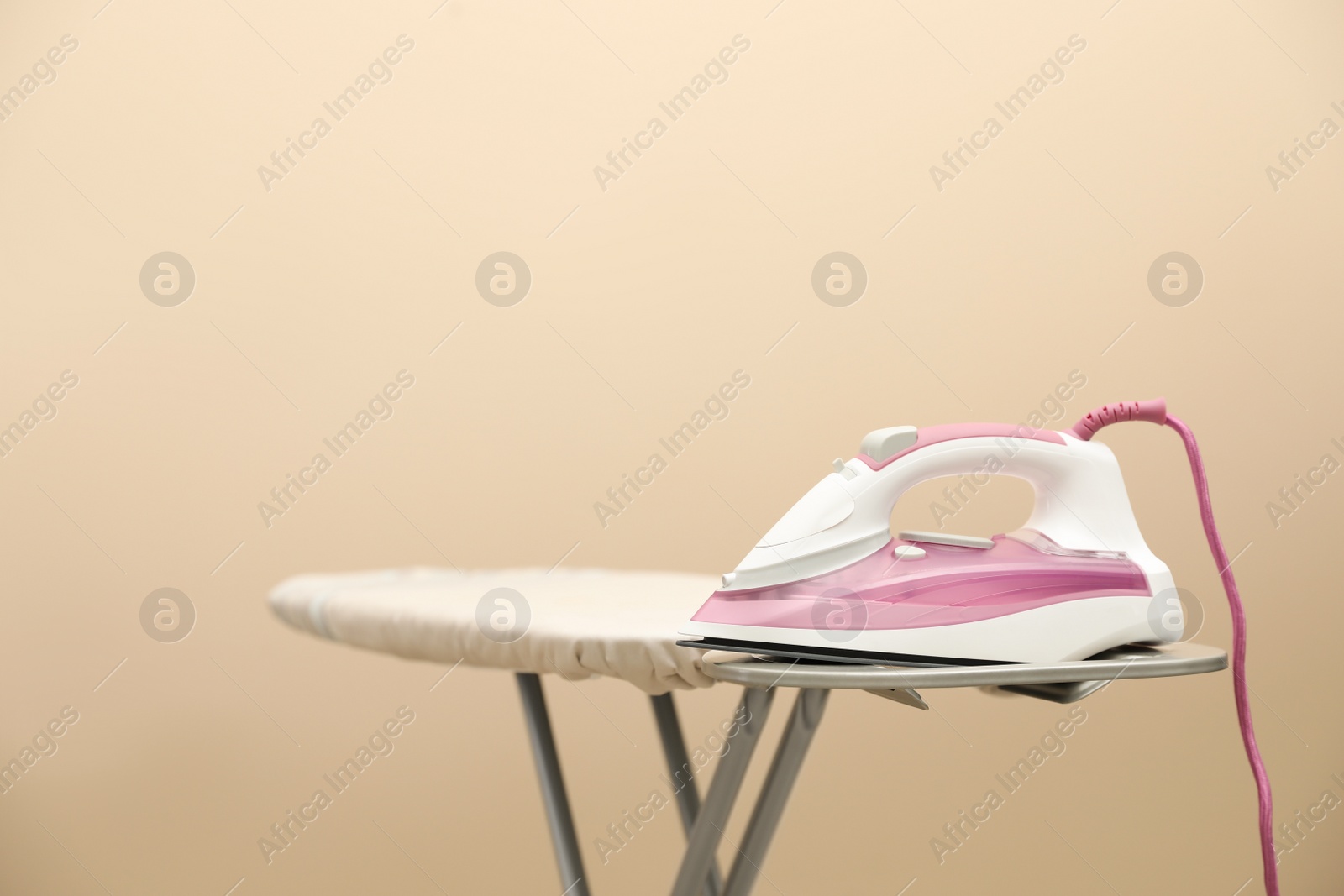 Photo of New modern iron on board against beige background, space for text