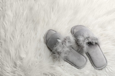 Photo of Pair of soft slippers on white faux fur, flat lay. Space for text