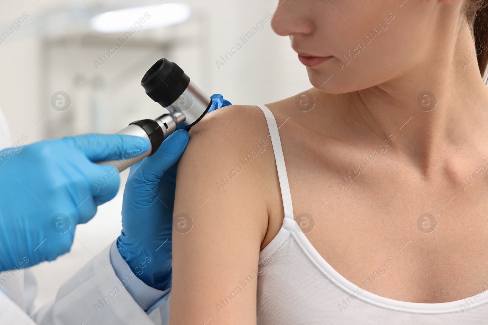 Photo of Dermatologist with dermatoscope examining patient in clinic, closeup