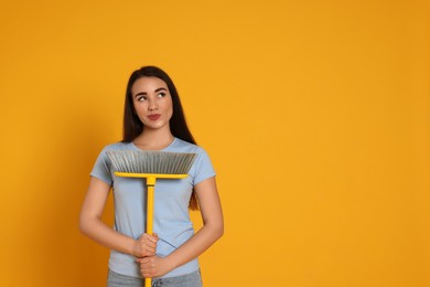 Photo of Beautiful young woman with broom on yellow background. Space for text