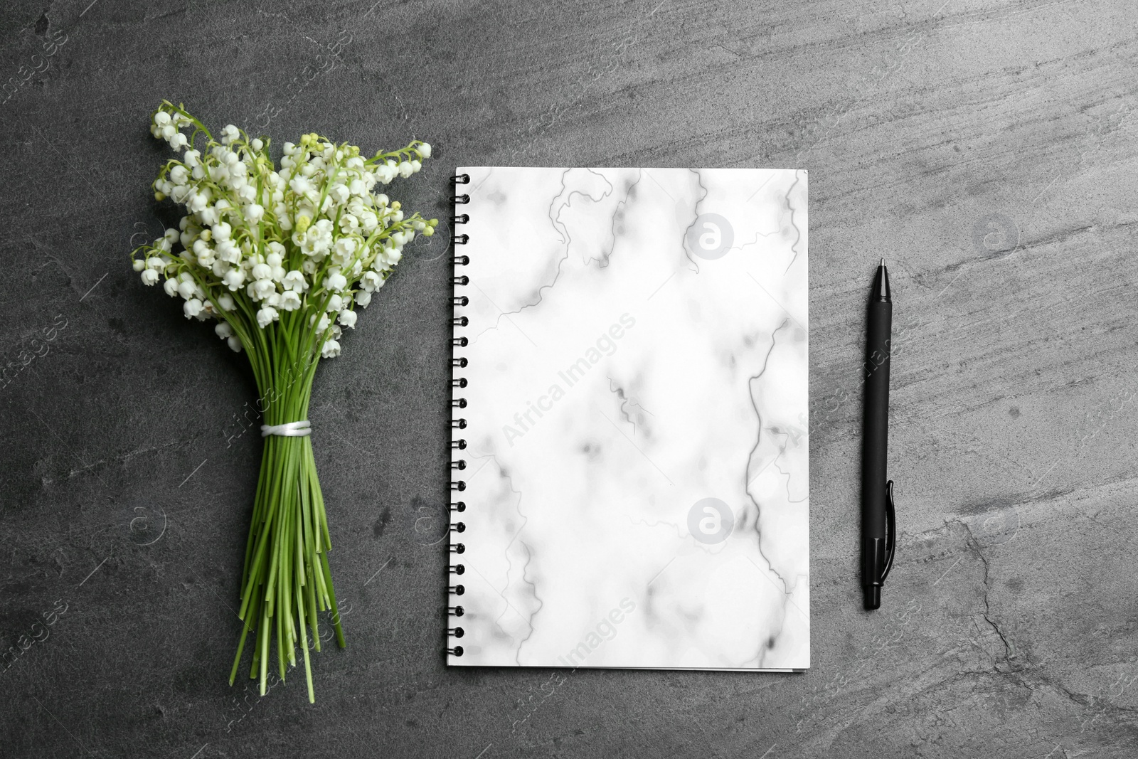 Photo of Notebook, pen and lily of the valley bouquet on grey background, flat lay. Space for text