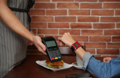 Woman using terminal for contactless payment with smart watch in cafe, closeup