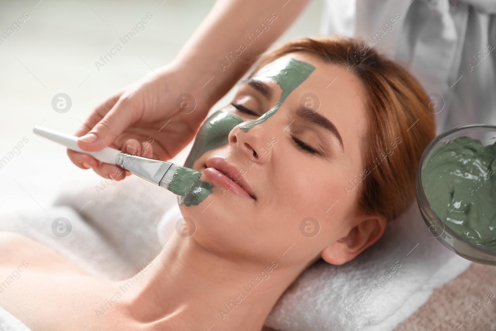 Photo of Cosmetologist applying mask onto woman's face in spa salon