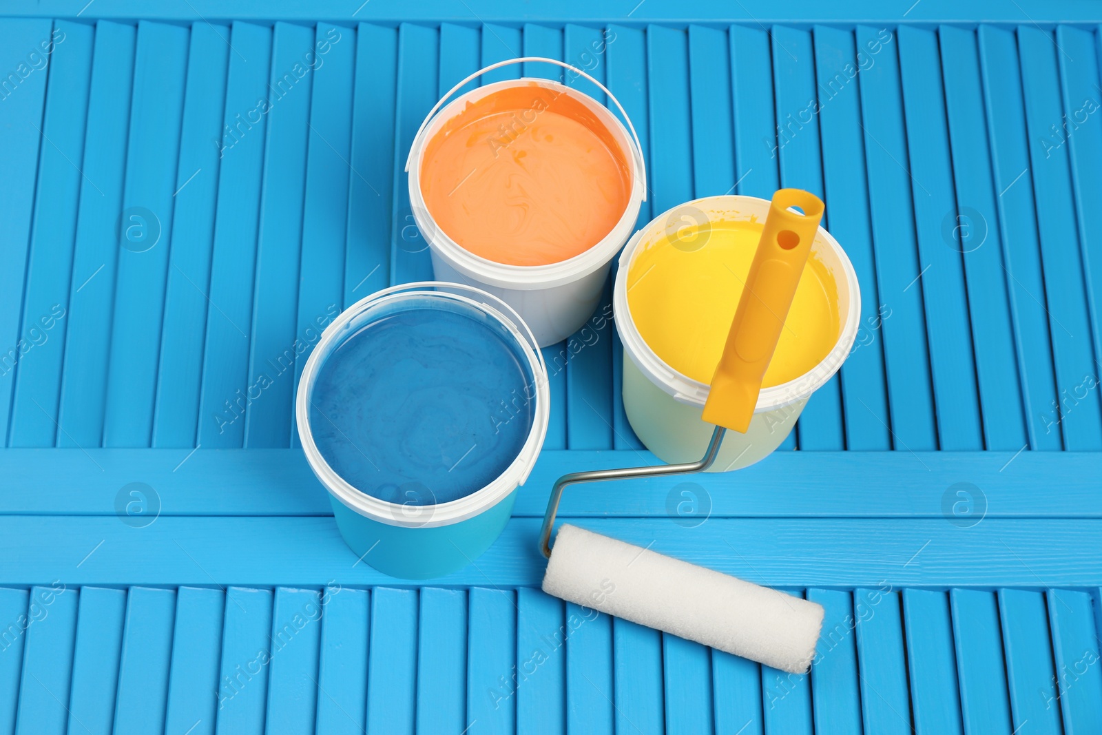 Photo of Buckets of paints and roller on light blue wooden background, above view