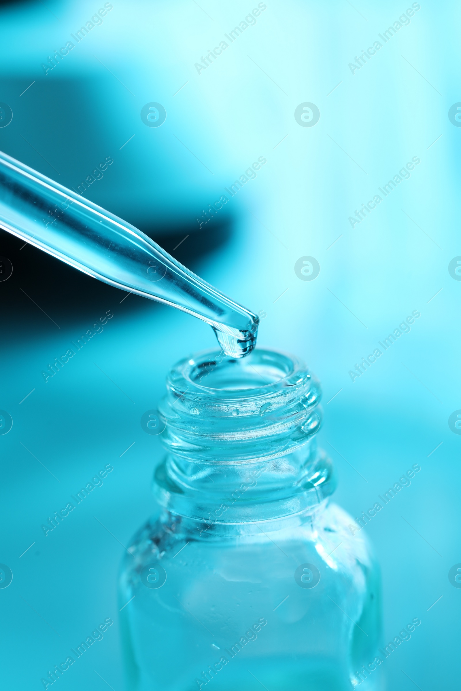 Photo of Dripping liquid from pipette into glass bottle on light blue background, closeup