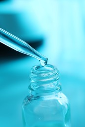 Dripping liquid from pipette into glass bottle on light blue background, closeup