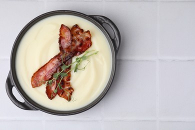 Photo of Delicious potato soup with bacon and microgreens in bowl on white tiled table, top view. Space for text