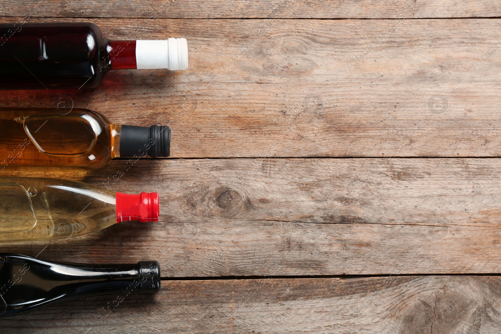 Photo of Bottles with different kinds of vinegar and space for text on wooden background, flat lay