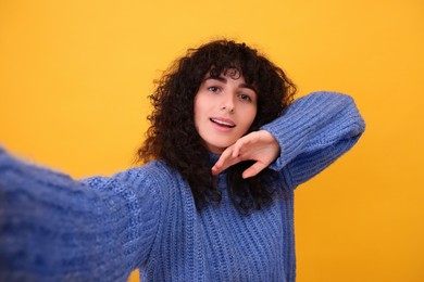 Photo of Beautiful young woman taking selfie on orange background