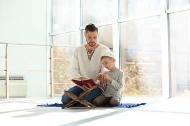 Photo of Muslim man and his son reading Koran together indoors