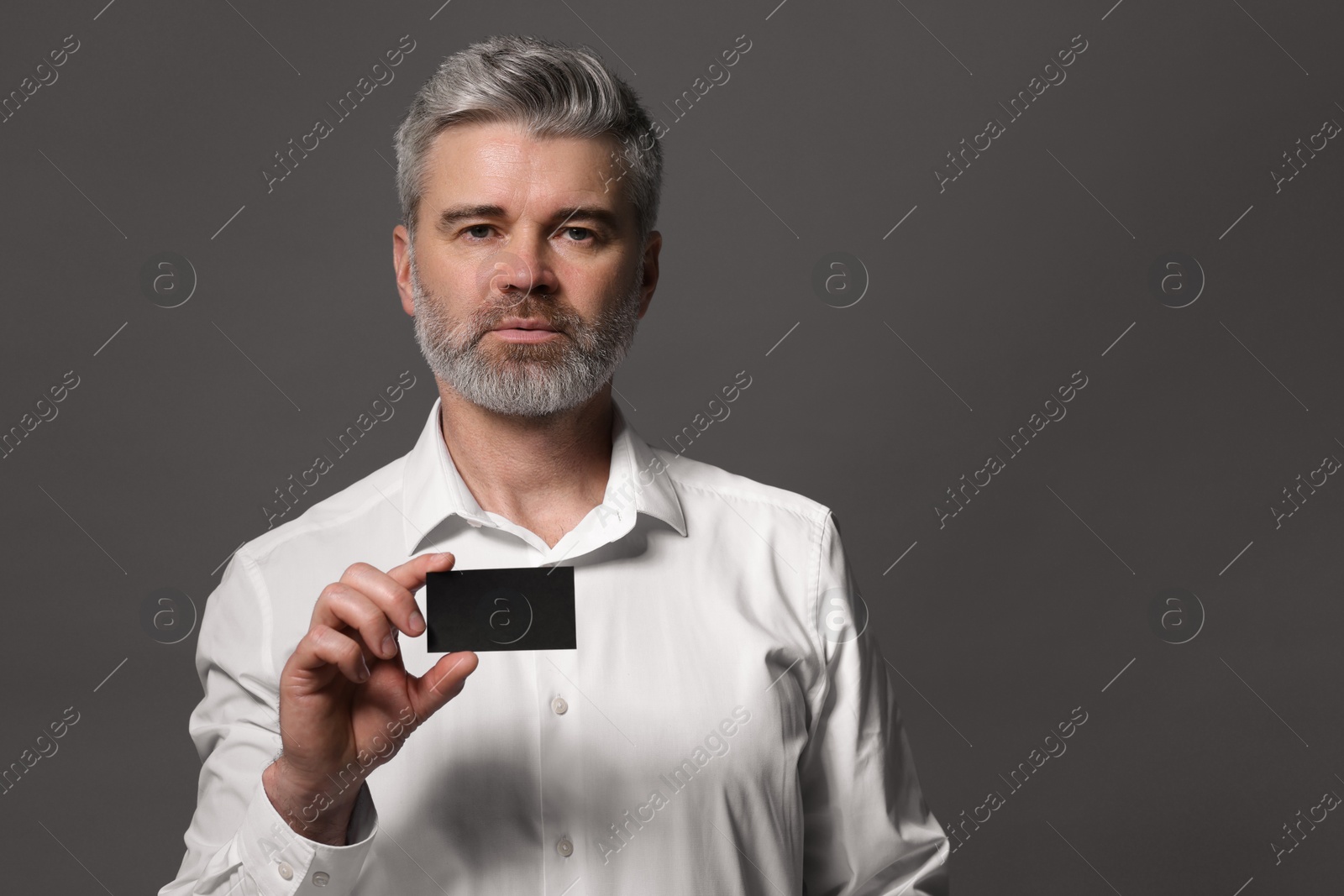 Photo of Handsome man holding blank business card on grey background. Space for text