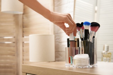 Photo of Woman taking lip gloss from organizer for makeup cosmetic products on table