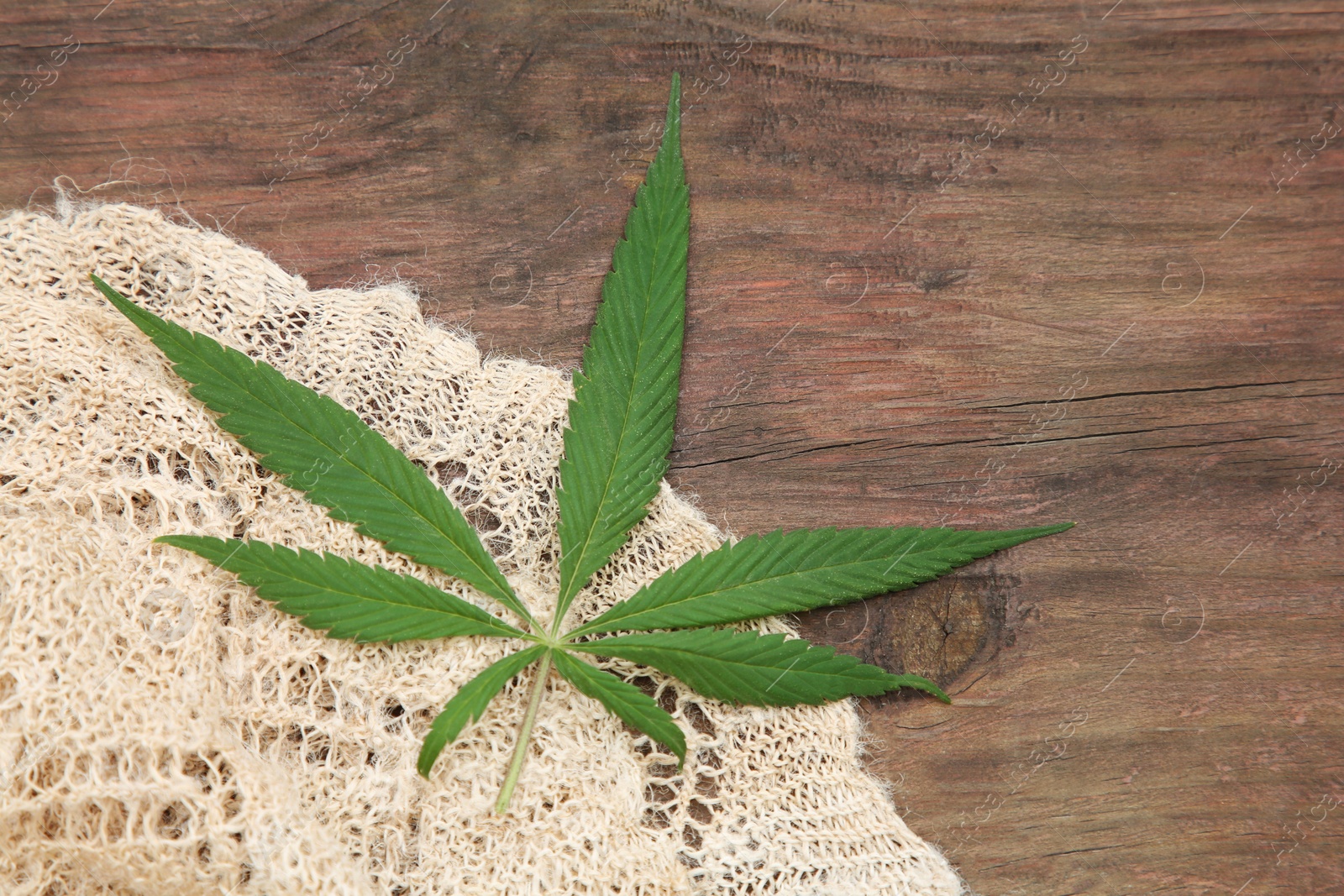 Photo of Hemp cloth and green leaf on wooden table, top view. Space for text