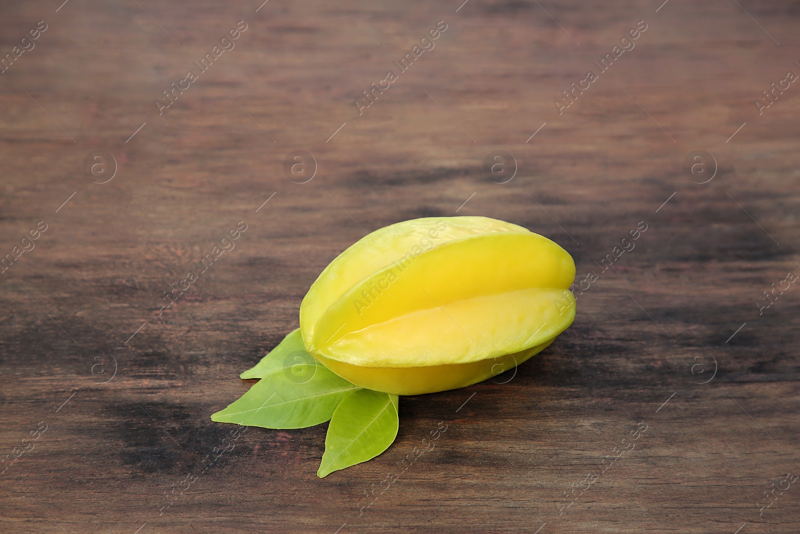 Photo of Delicious ripe carambola with leaves on wooden table